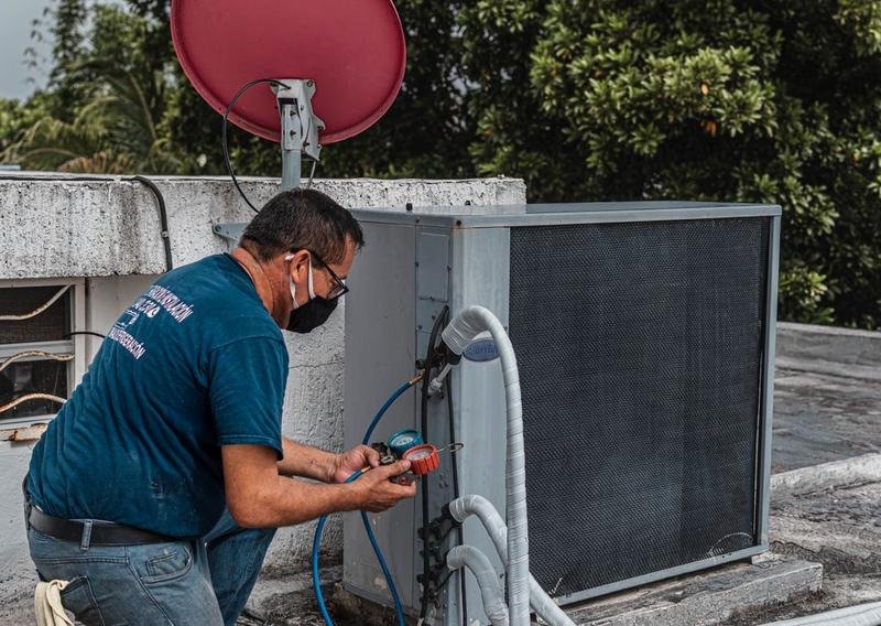 AC technician servicing an outdoor unit with manifold gauges